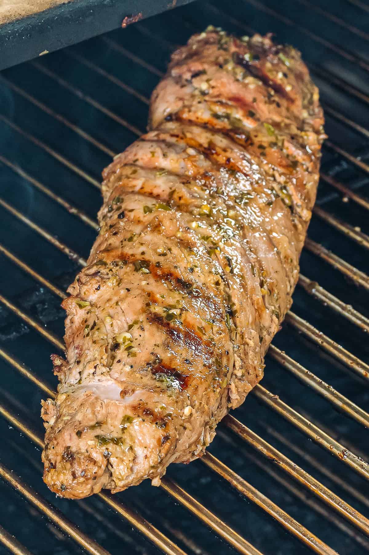 Pork tenderloin grilling on a hot grill until browned.