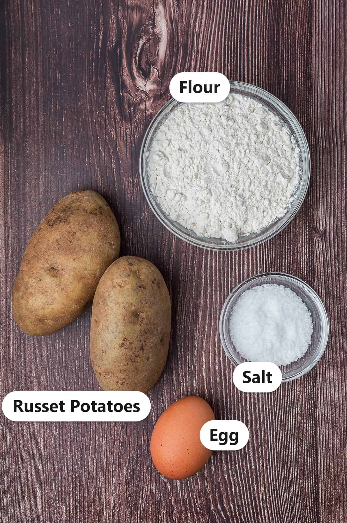 Labeled ingredients for homemade potato gnocchi including russet potatoes, flour, salt, and an egg.