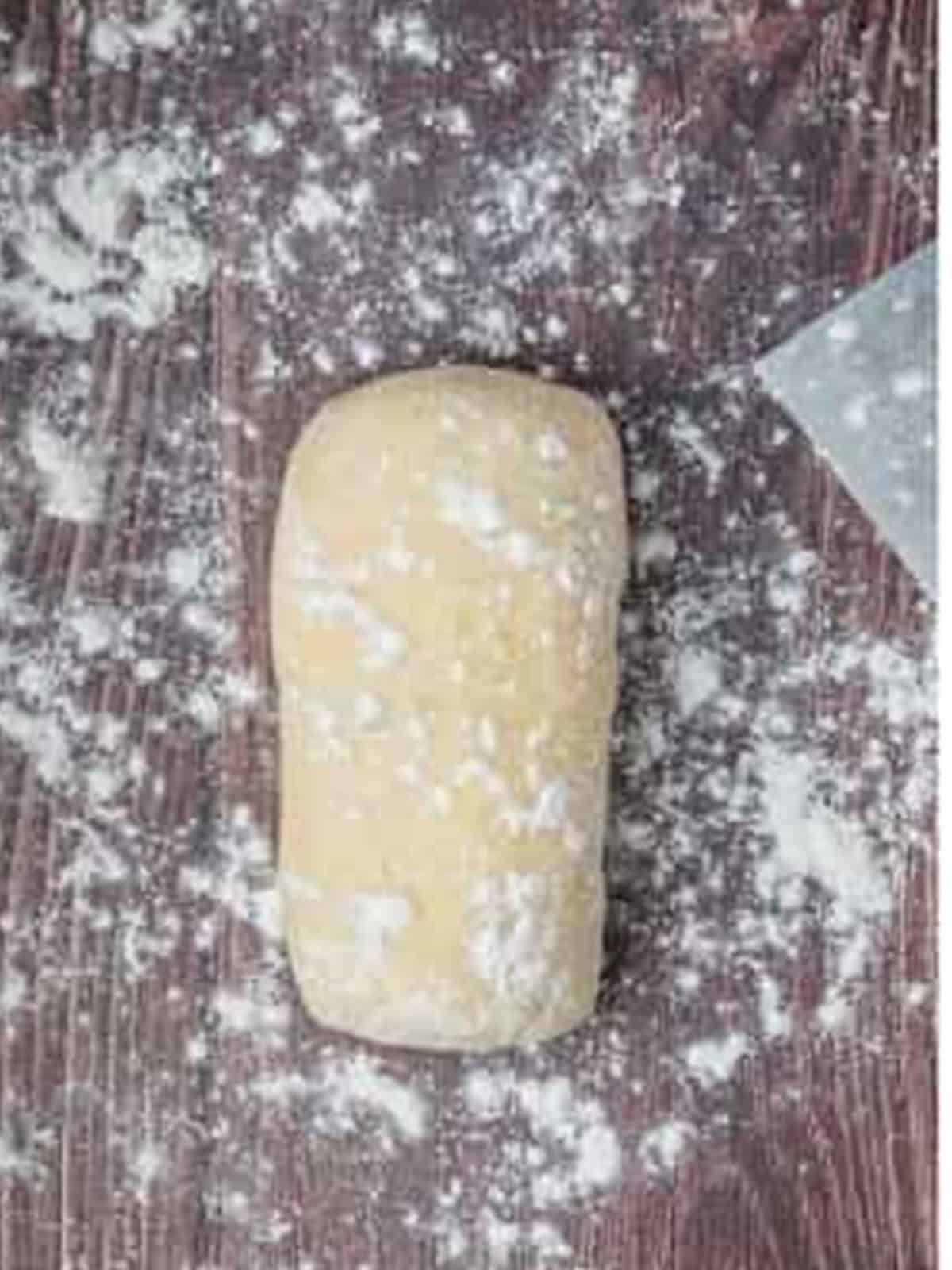 Potato gnocchi dough formed into a smooth log on a floured surface.