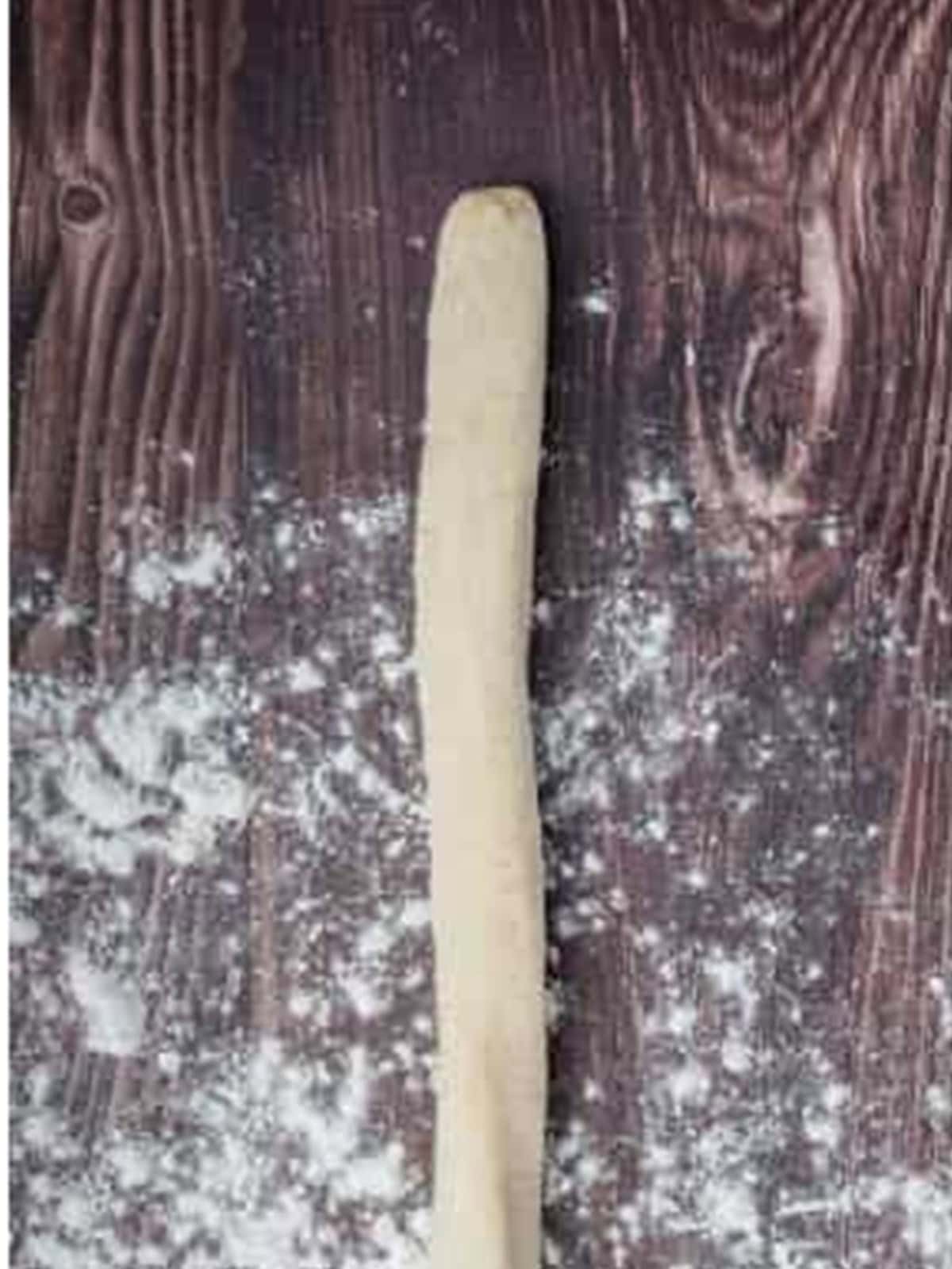 Potato gnocchi dough rolled into a long thin rope on a floured board.