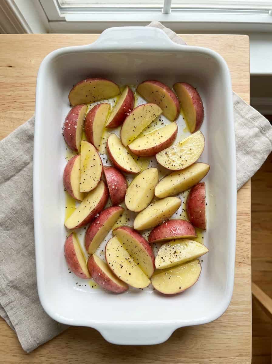 Raw red potato wedges tossed with oil, salt, and pepper in a baking dish.