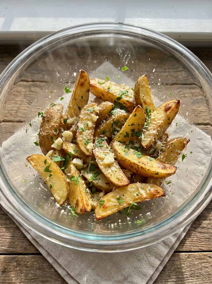Grilled potato wedges tossed with garlic butter and parsley in a glass bowl.