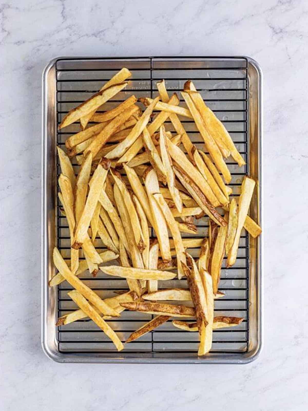 Blanched poutine fries draining on a wire cooling rack.