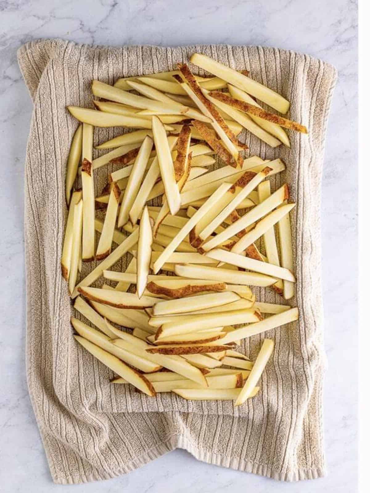 Russet potatoes cut into fries on a towel-lined tray for poutine.