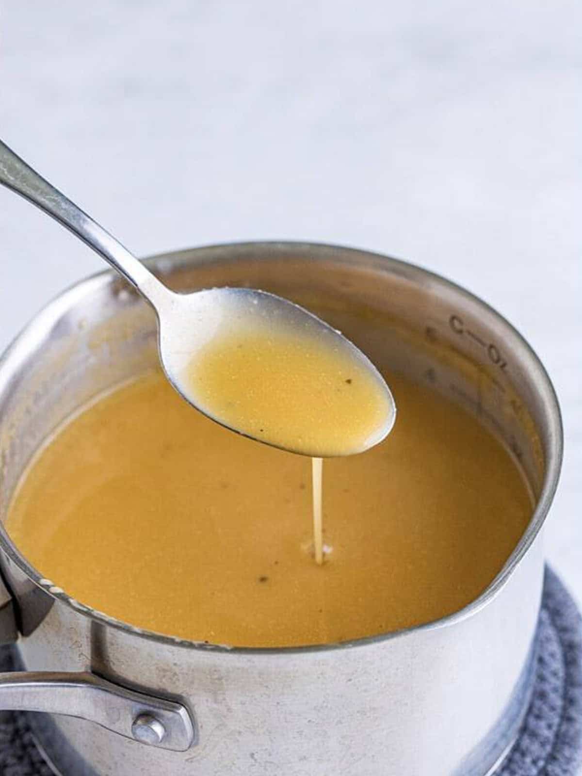 Homemade brown gravy for poutine in a saucepan with a spoon.