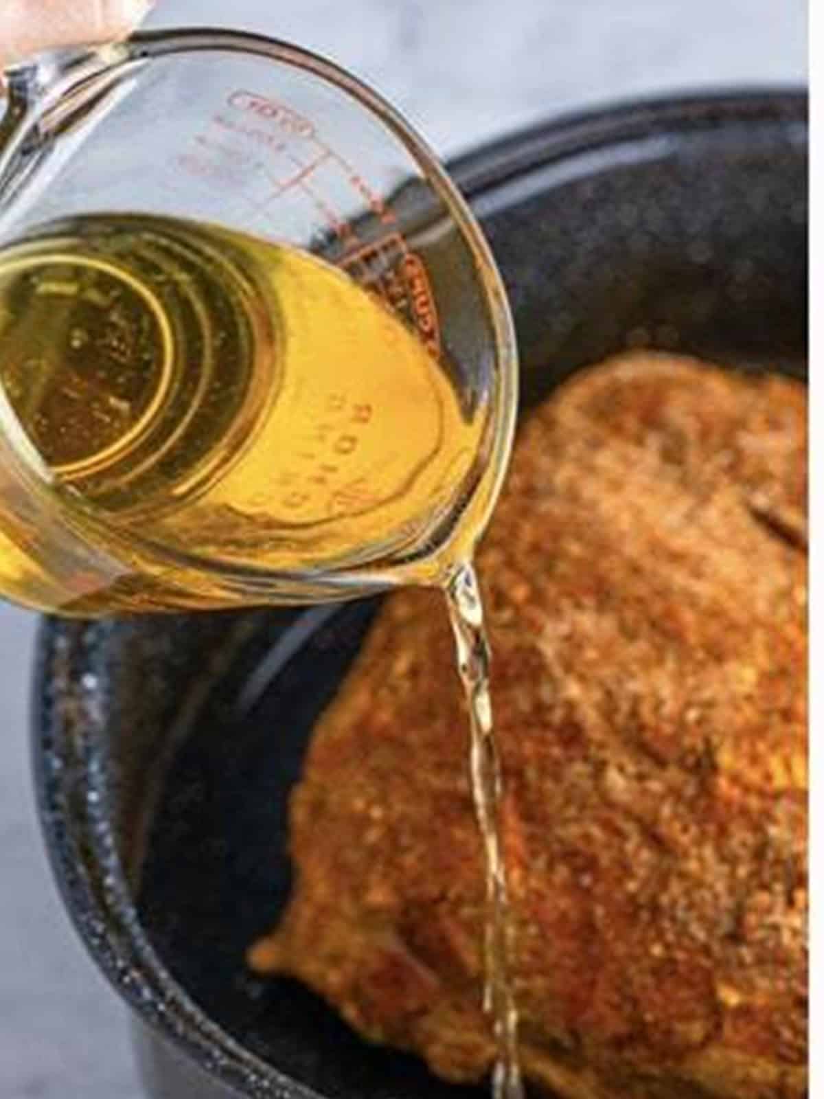 Beer poured around the seasoned pork shoulder in a roasting pan.