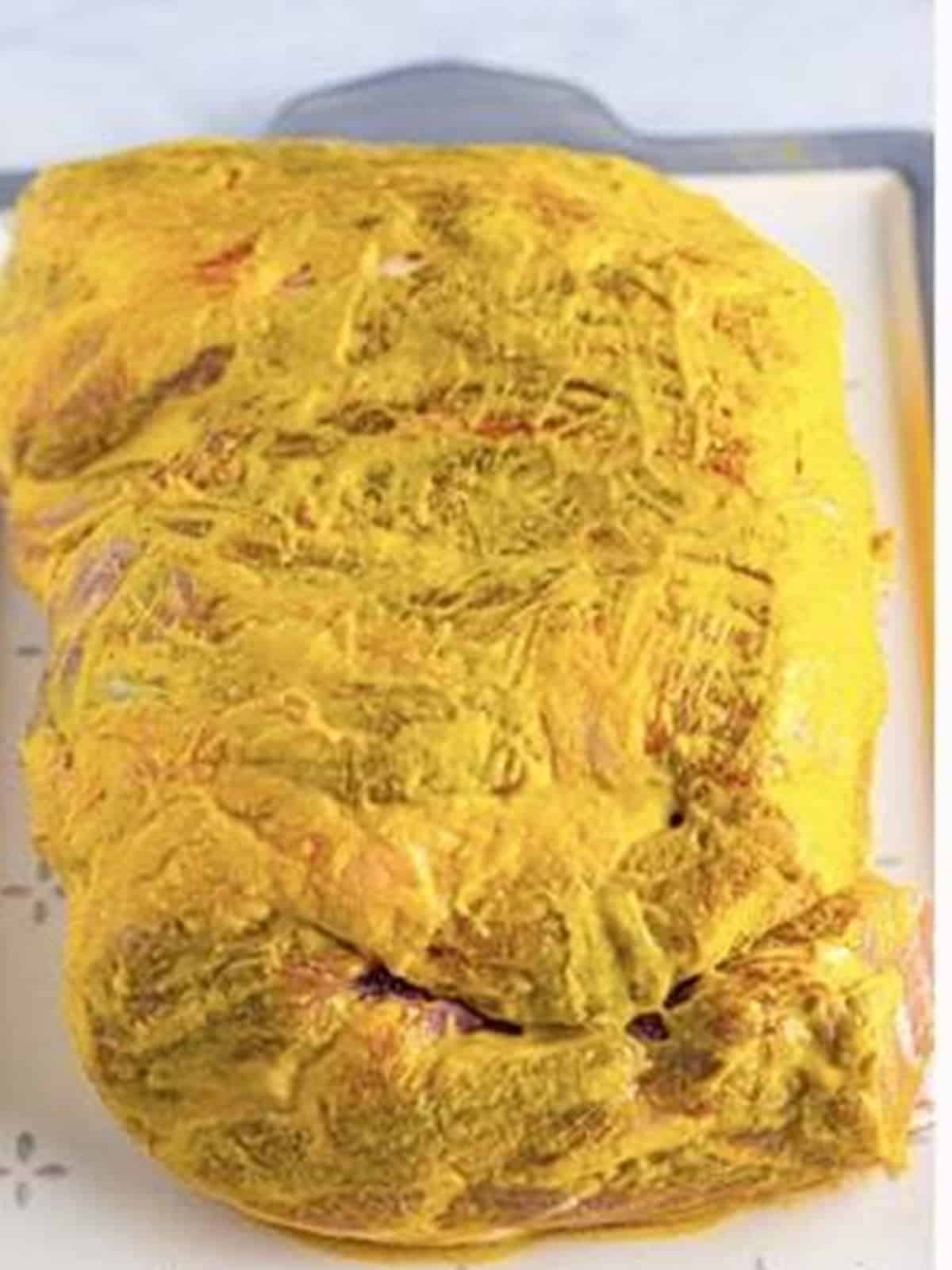 A pork shoulder brushed all over with yellow mustard for pulled pork.
