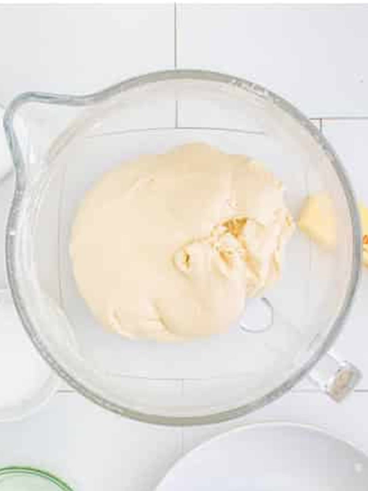 Pretzel dough coming together in a large glass mixing bowl.