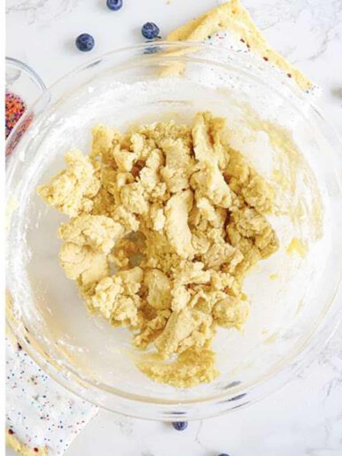 A soft sugar cookie dough formed in a glass mixing bowl.