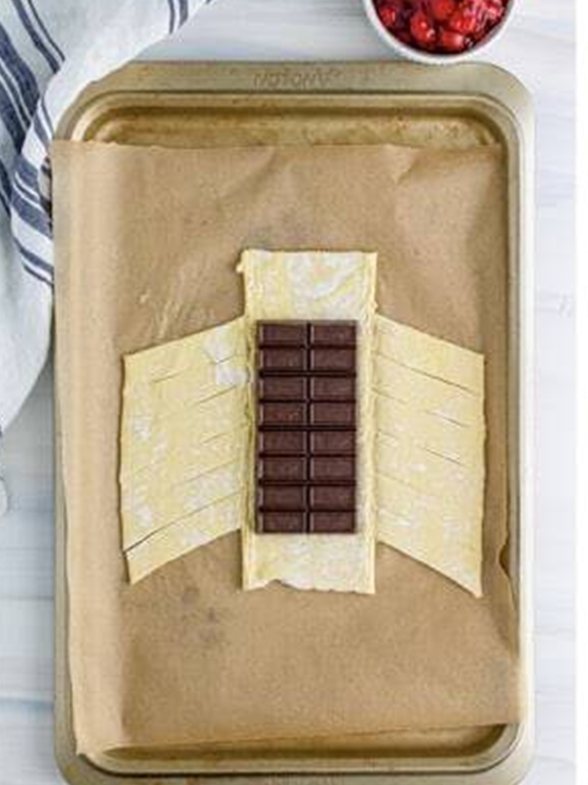 Chocolate bar placed on puff pastry with diagonal slits cut down the sides.