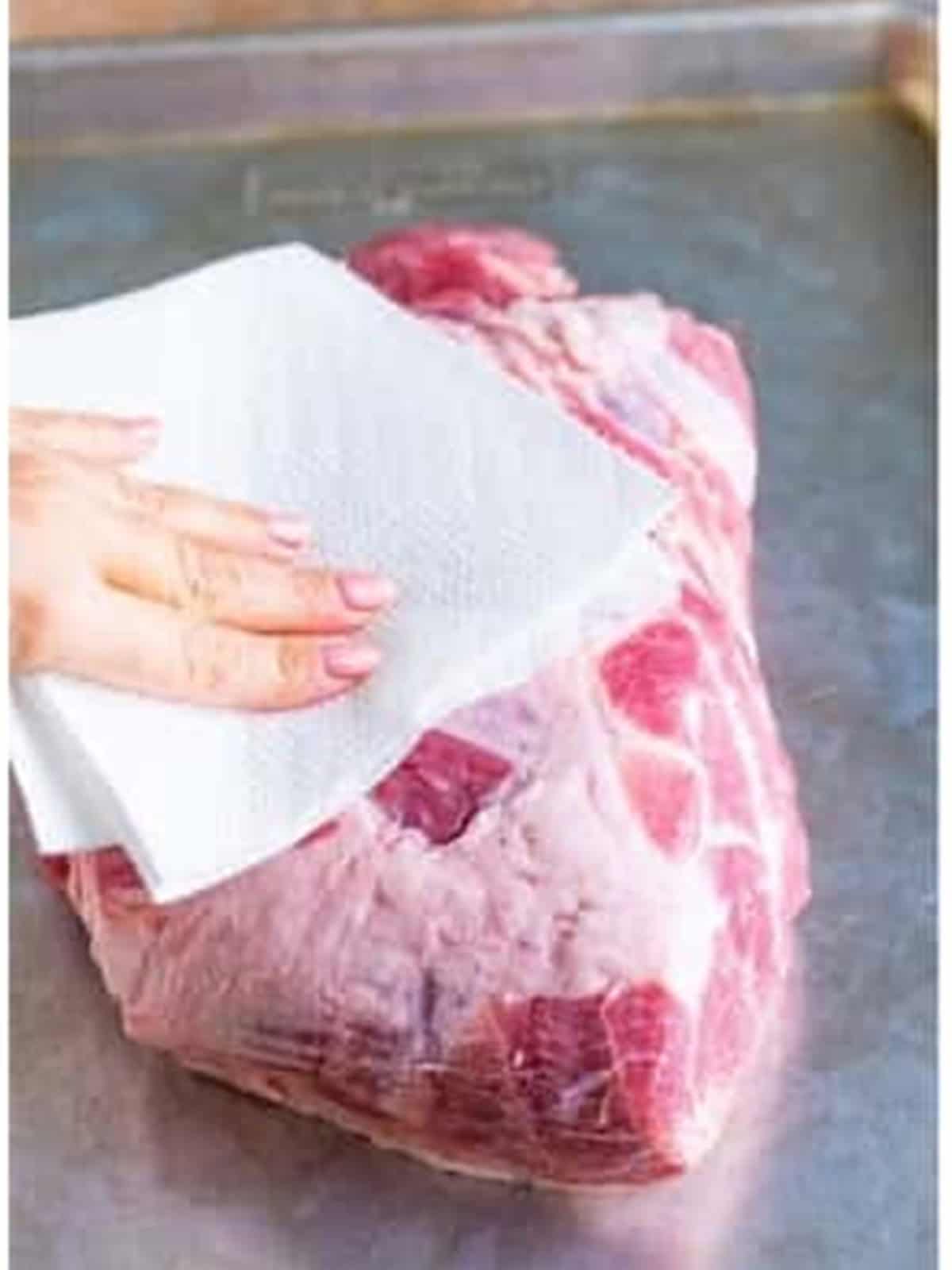 Patting a pork shoulder dry with paper towels for the pulled pork recipe.