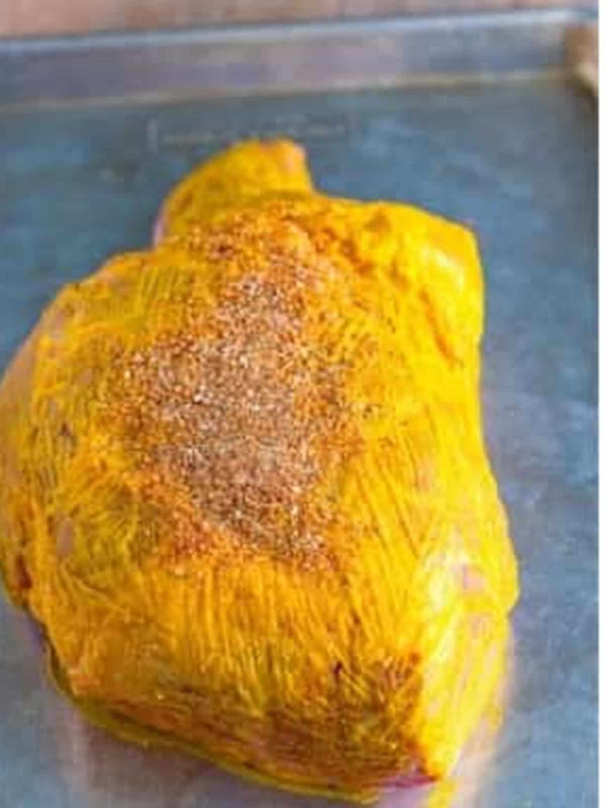 Patting the spice rub onto the mustard-coated pork shoulder for the pulled pork recipe.