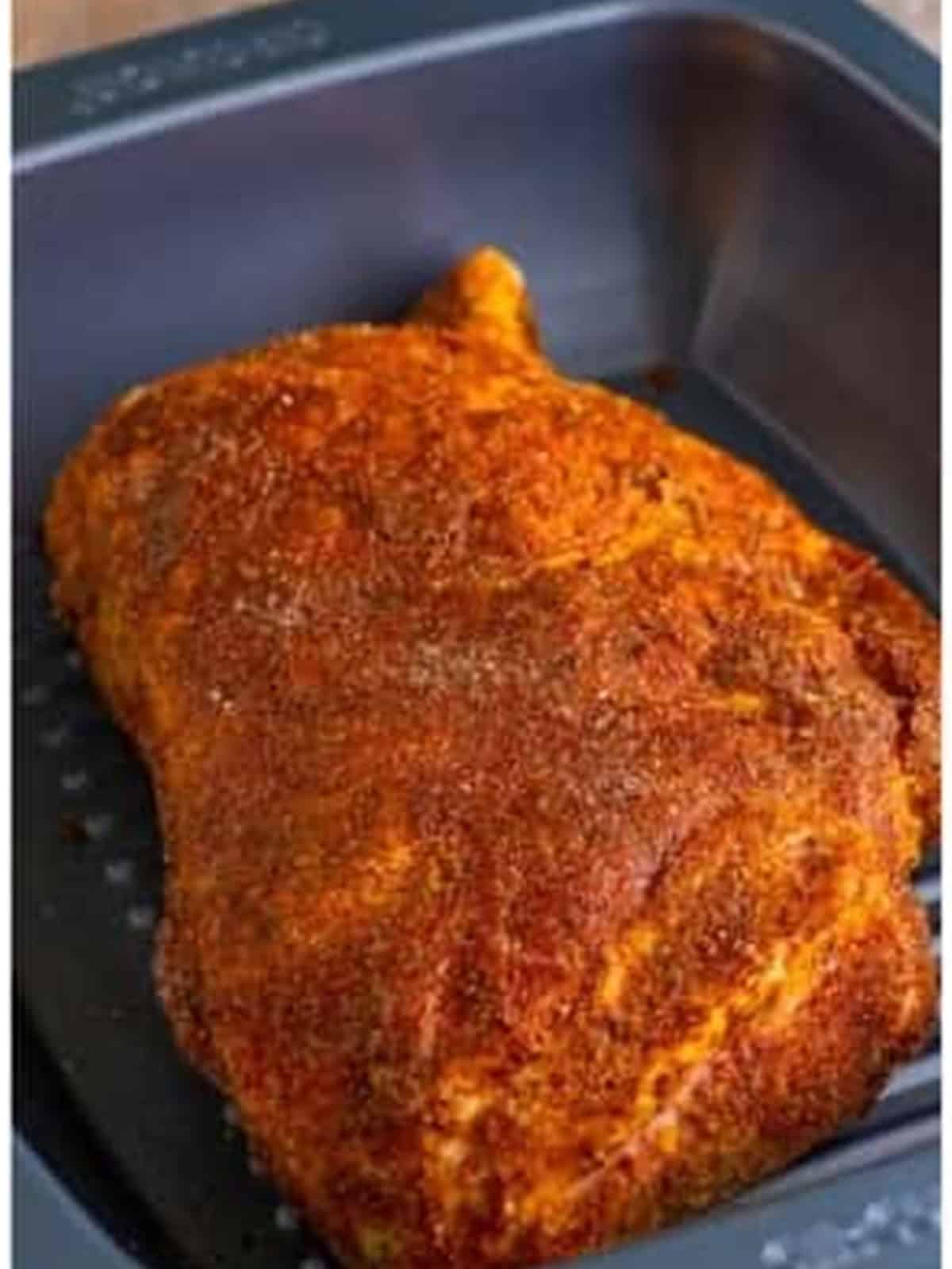 The seasoned pork shoulder fully coated in spice rub and placed in a roasting pan for the pulled pork recipe.