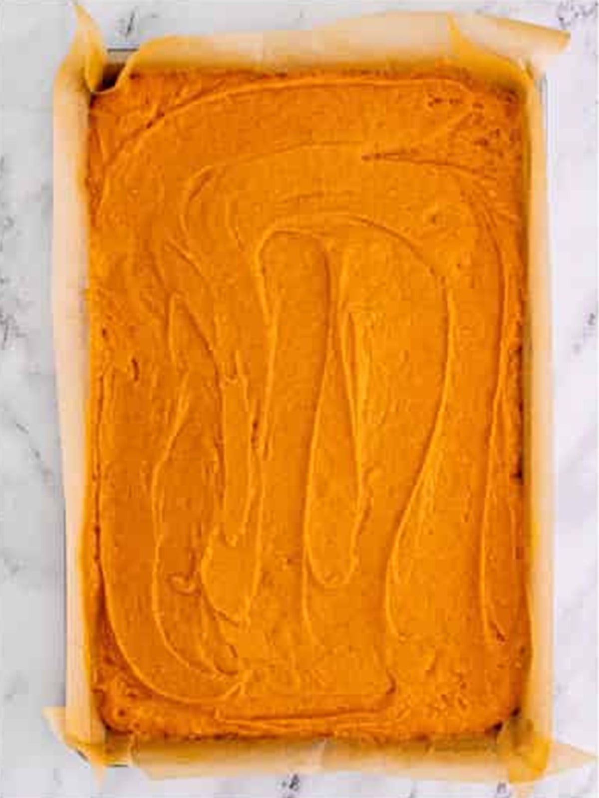 Spreading the pumpkin bar batter evenly in a parchment-lined pan.