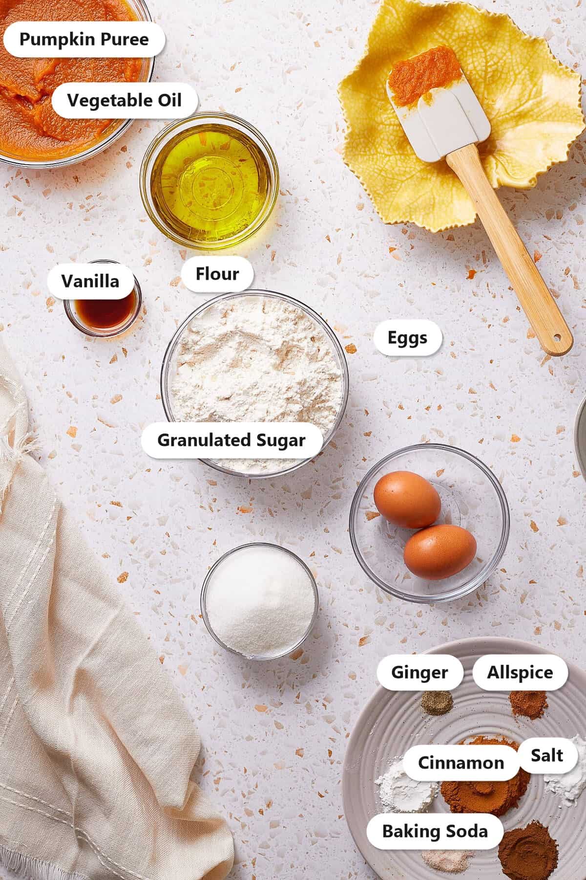 Labeled ingredients to make pumpkin bundt cake including pumpkin puree, flour, vegetable oil, eggs, granulated sugar, and warm baking spices.