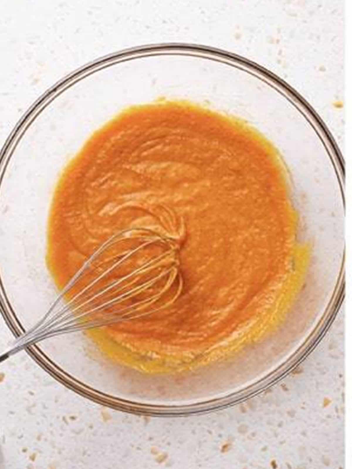 Mixing the wet pumpkin batter ingredients including oil, sugar, eggs, and pumpkin puree.