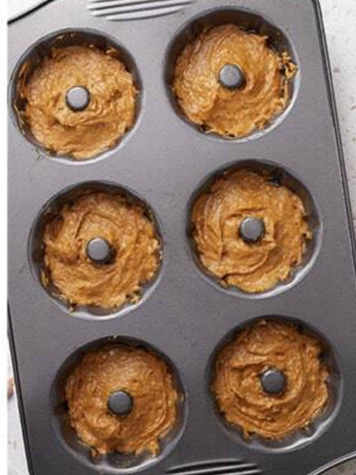 Pumpkin bundt cake batter divided into a greased mini bundt cake pan.