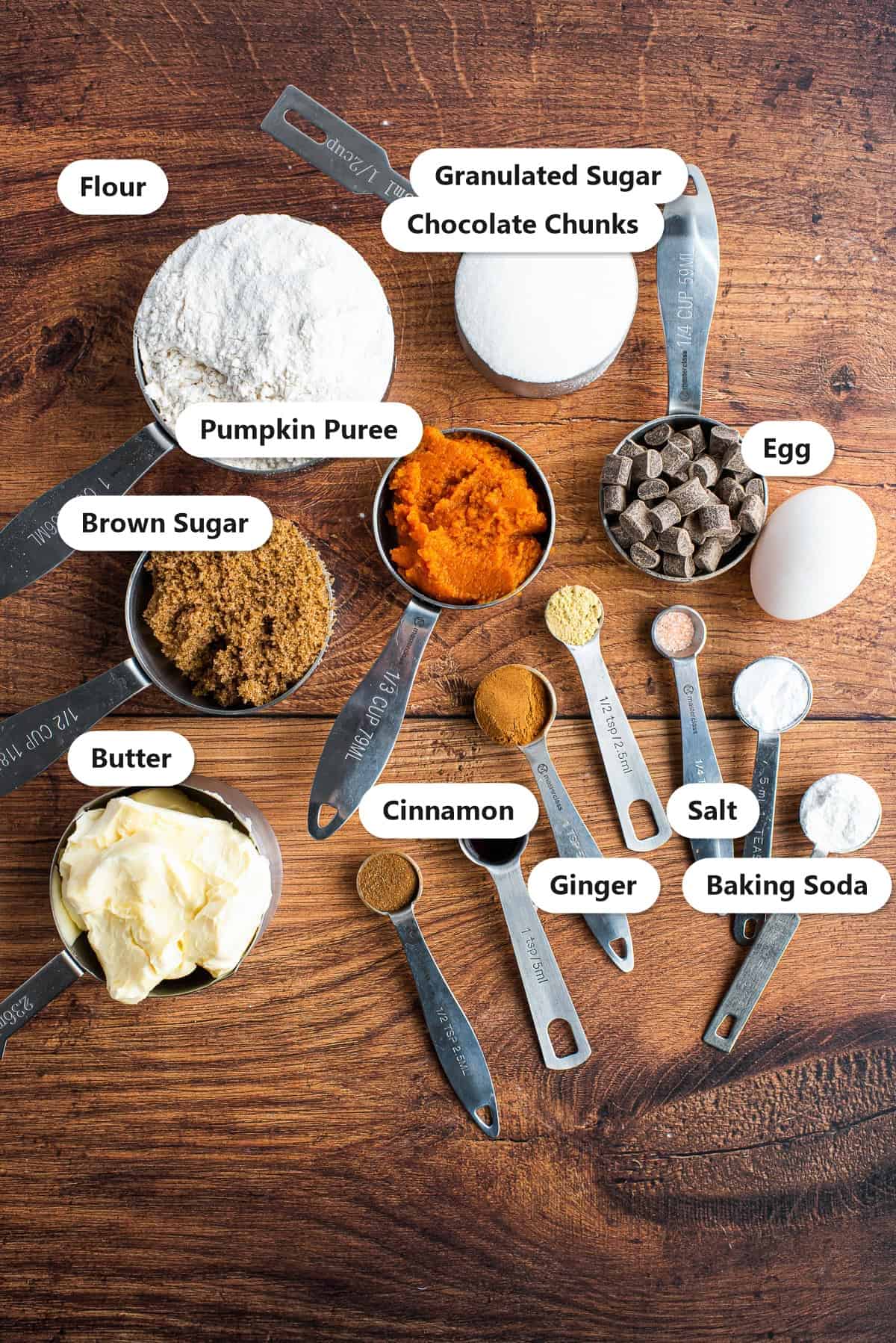 Labeled ingredients for pumpkin chocolate chip cookies including flour, sugar, brown sugar, pumpkin puree, butter, egg, chocolate chunks, cinnamon, ginger, and baking soda.