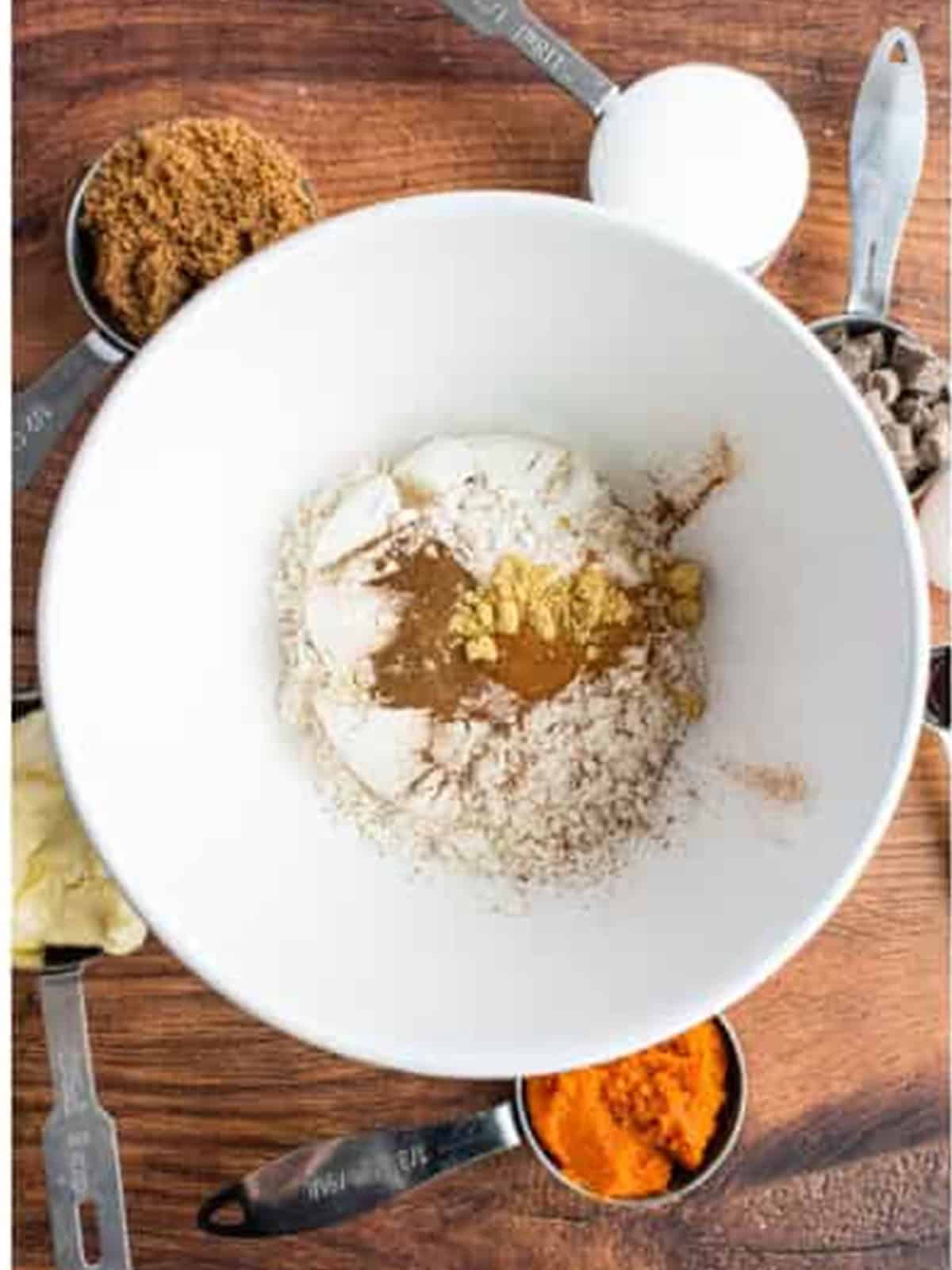 Whisking together flour, baking soda, salt, and pumpkin pie spices in a white bowl.
