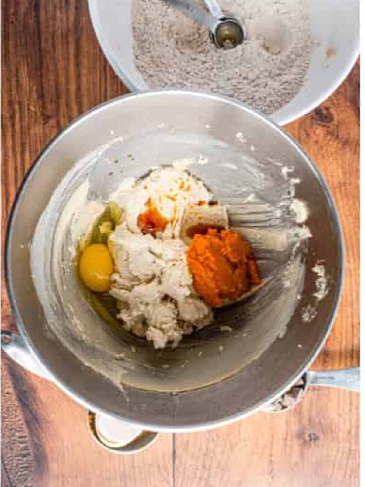 Adding egg and pumpkin puree to the creamed butter and sugar in a mixer.