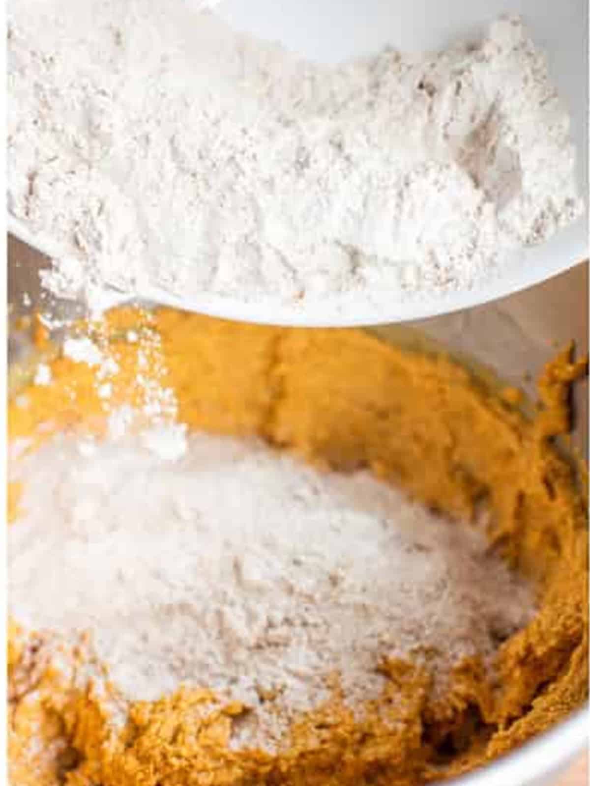Adding the flour mixture to the wet pumpkin batter in a mixing bowl.