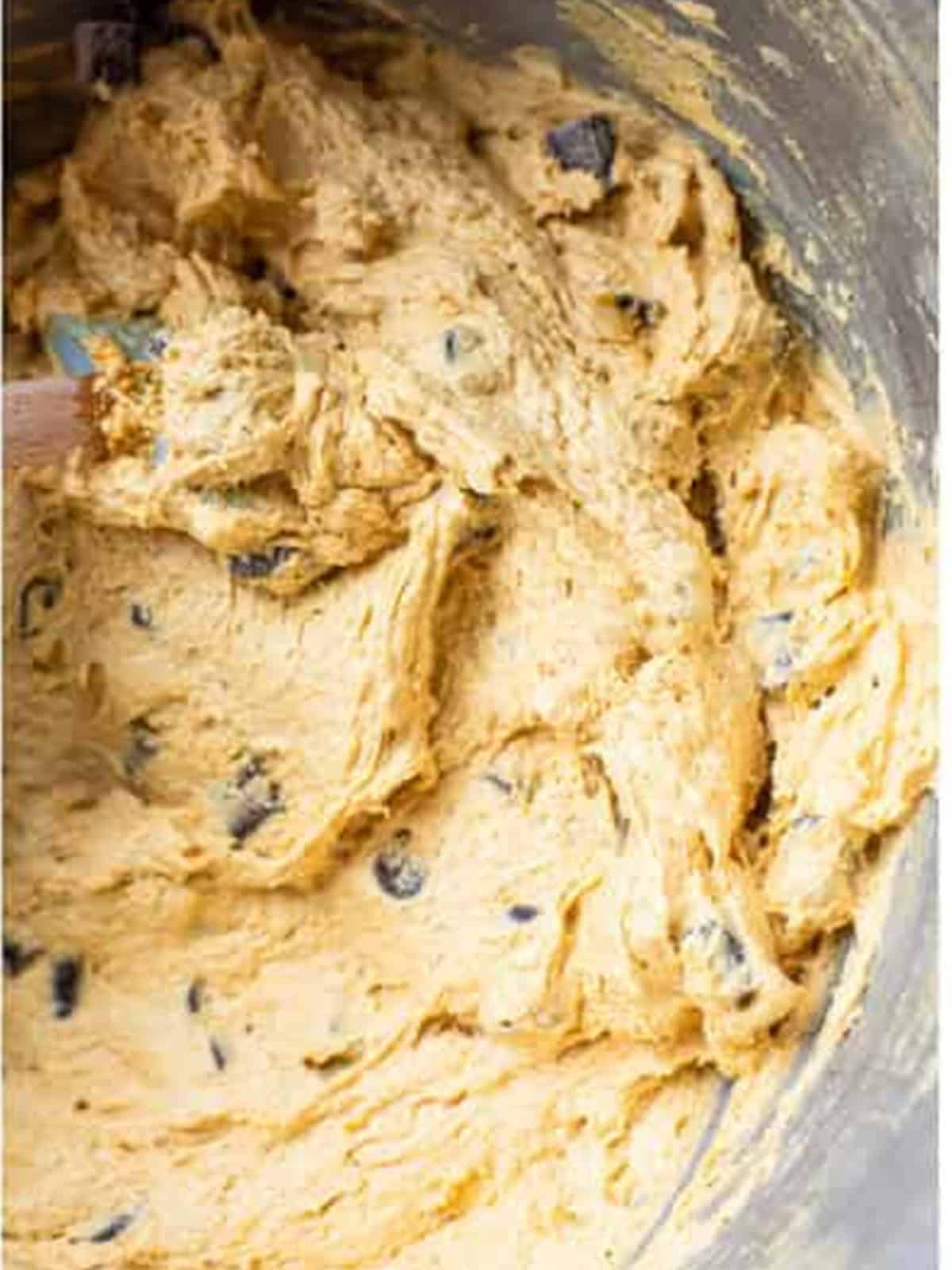 Folding chocolate chunks into the pumpkin cookie dough with a spatula.
