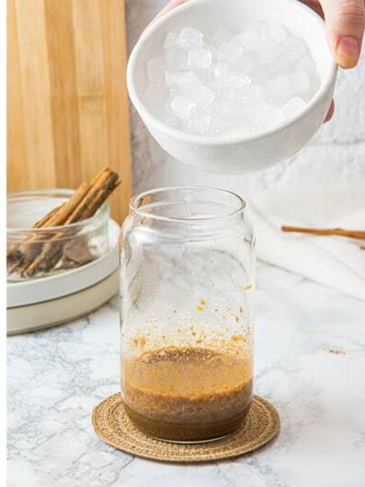 Ice being added to the frothy pumpkin spice latte base in a glass.
