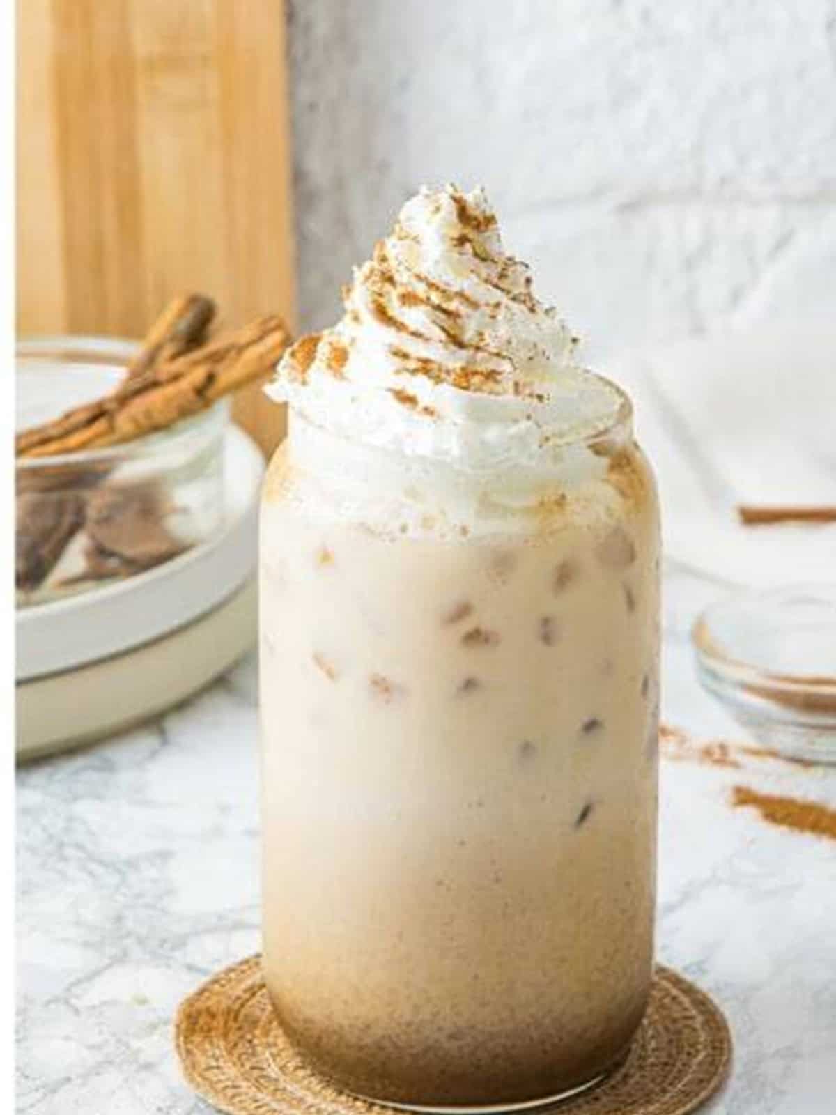 A finished iced pumpkin spice latte topped with whipped cream and a sprinkle of ground cinnamon.