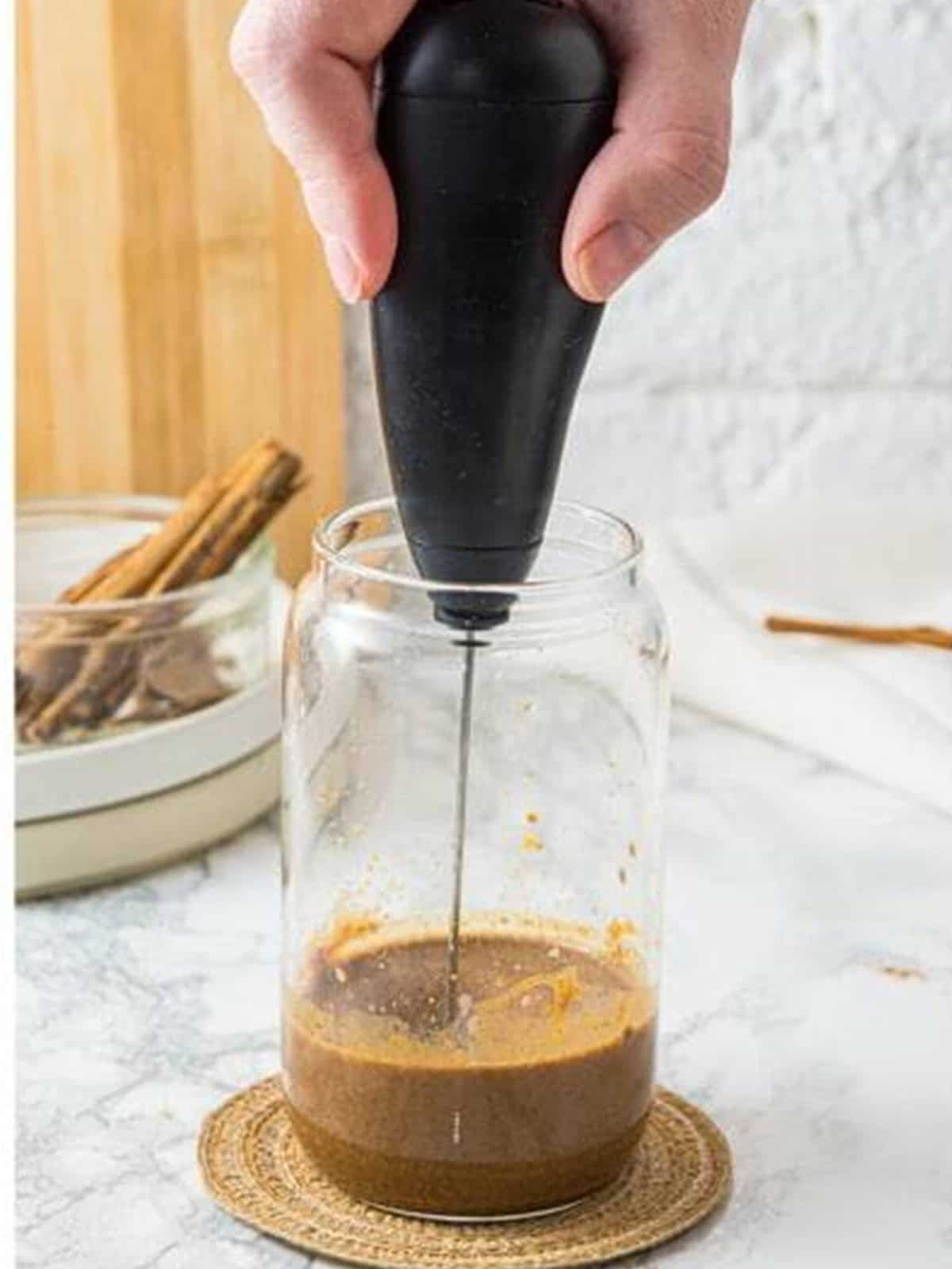 An electric frother whisking the pumpkin coffee base until frothy in a glass.
