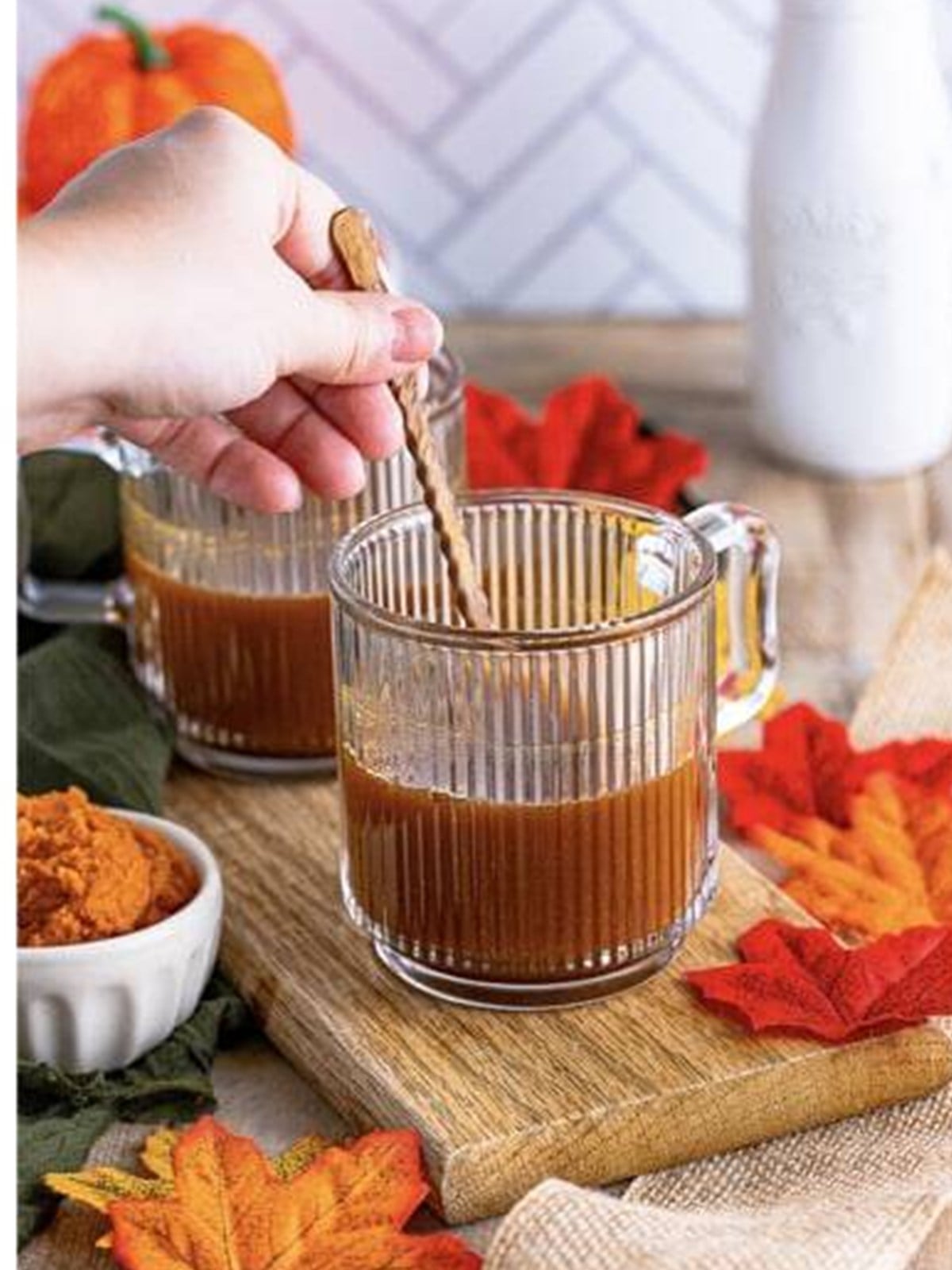 Pumpkin and coffee stirred together with a cinnamon stick in a glass mug.