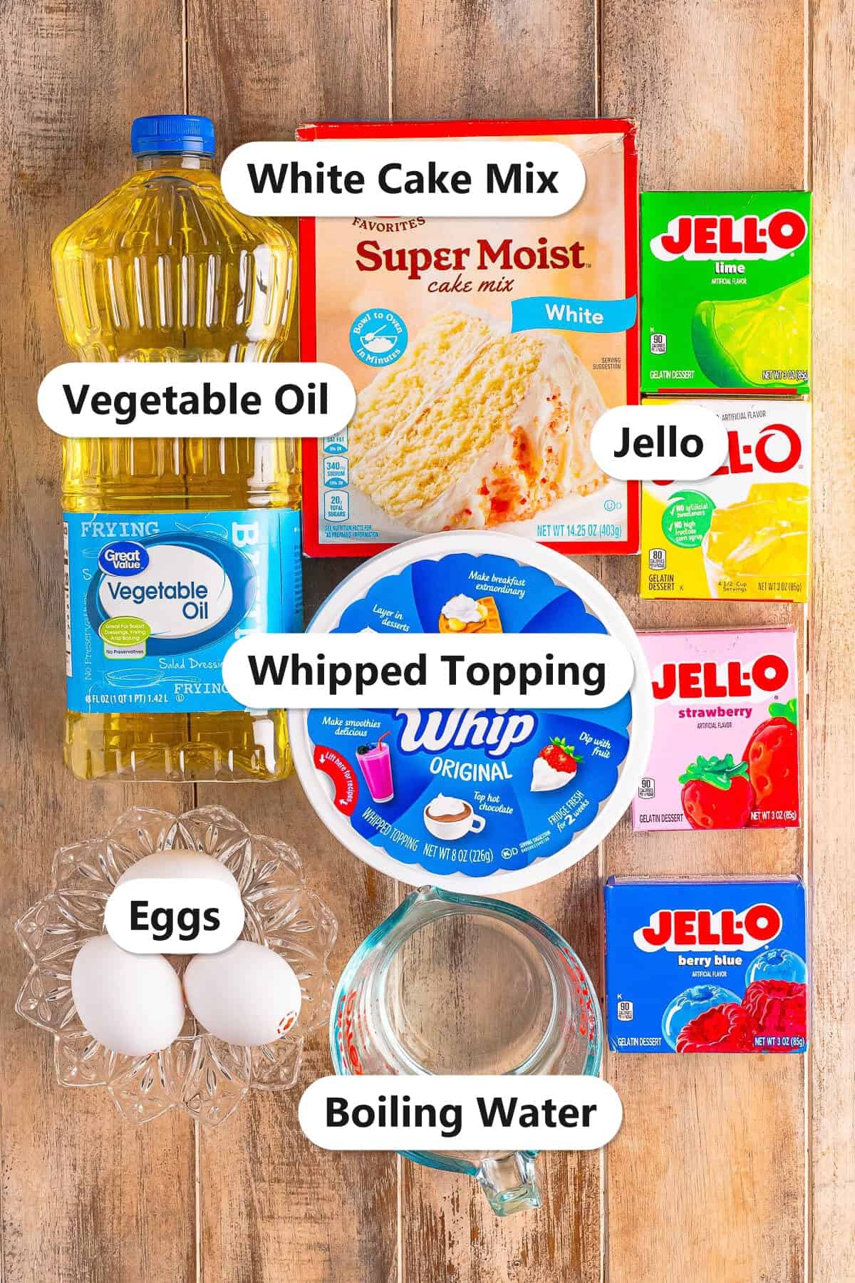 Labeled ingredients for rainbow jello cake including white cake mix, jello, whipped topping, oil, eggs, and water.