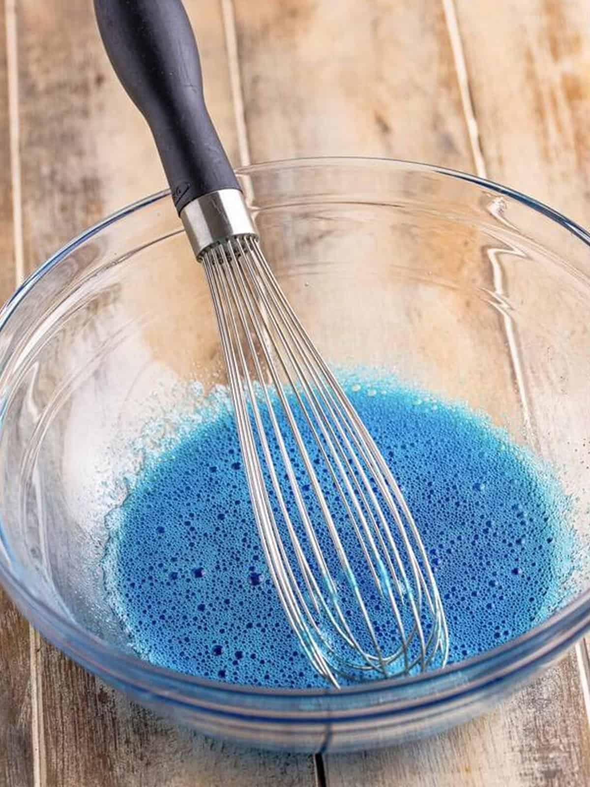 Blue jello being whisked into boiling water in a bowl.