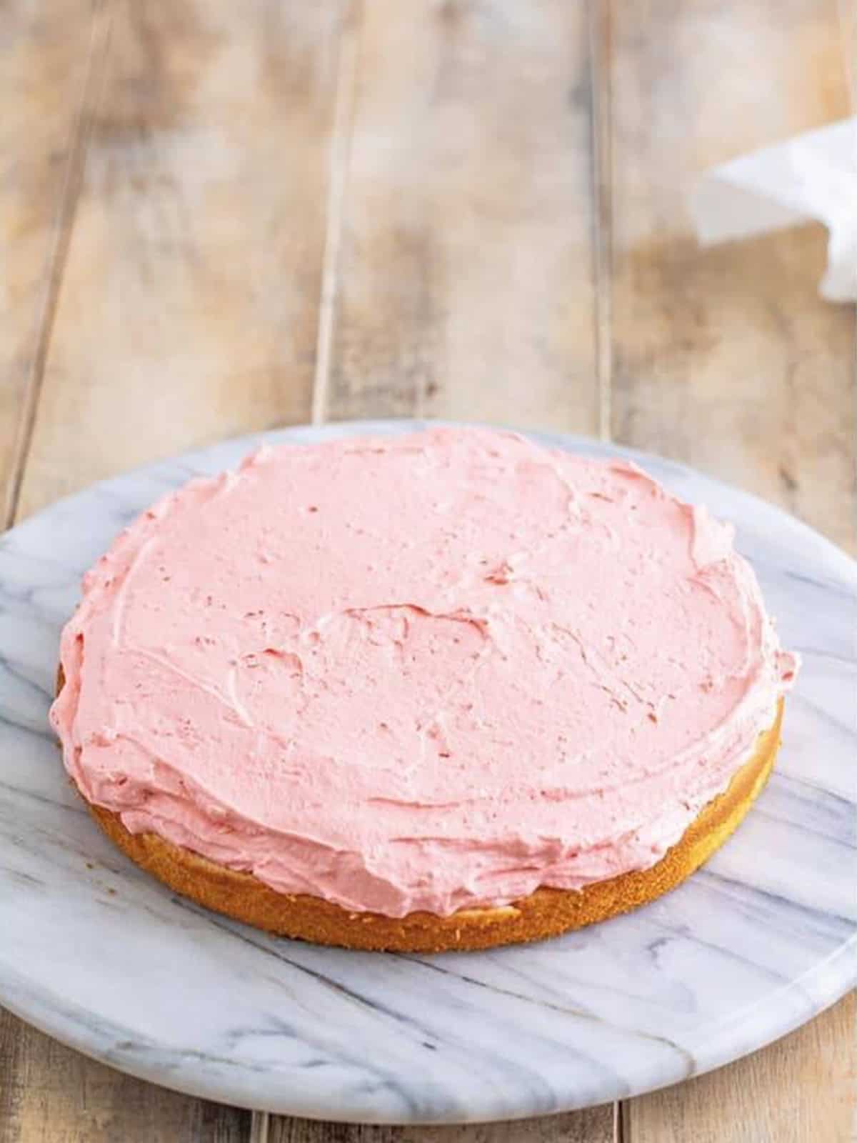Pink jello frosting spread over a cake layer for rainbow jello cake.