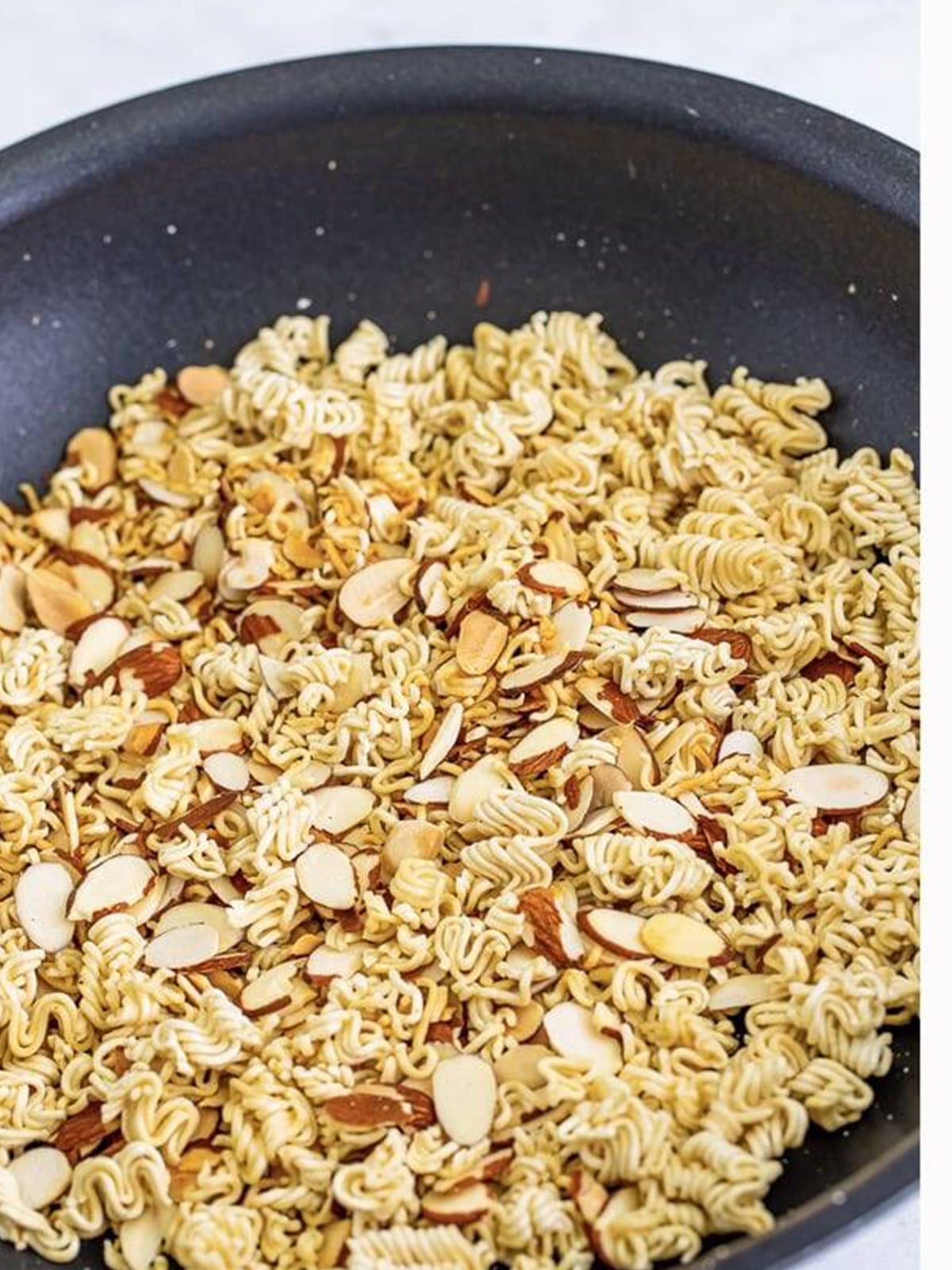 Crushed ramen noodles and sliced almonds toasted golden in a skillet.