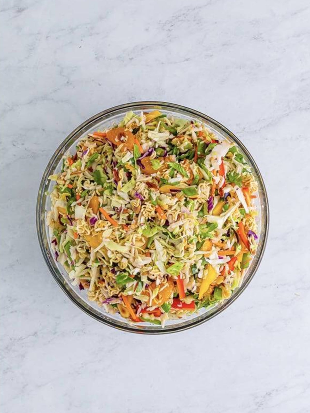 Crunchy Asian ramen noodle salad tossed with dressing in a glass bowl.