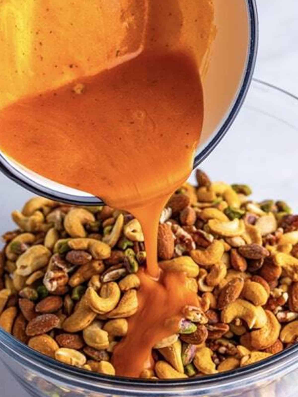 Buffalo butter sauce being poured over a bowl of mixed nuts.