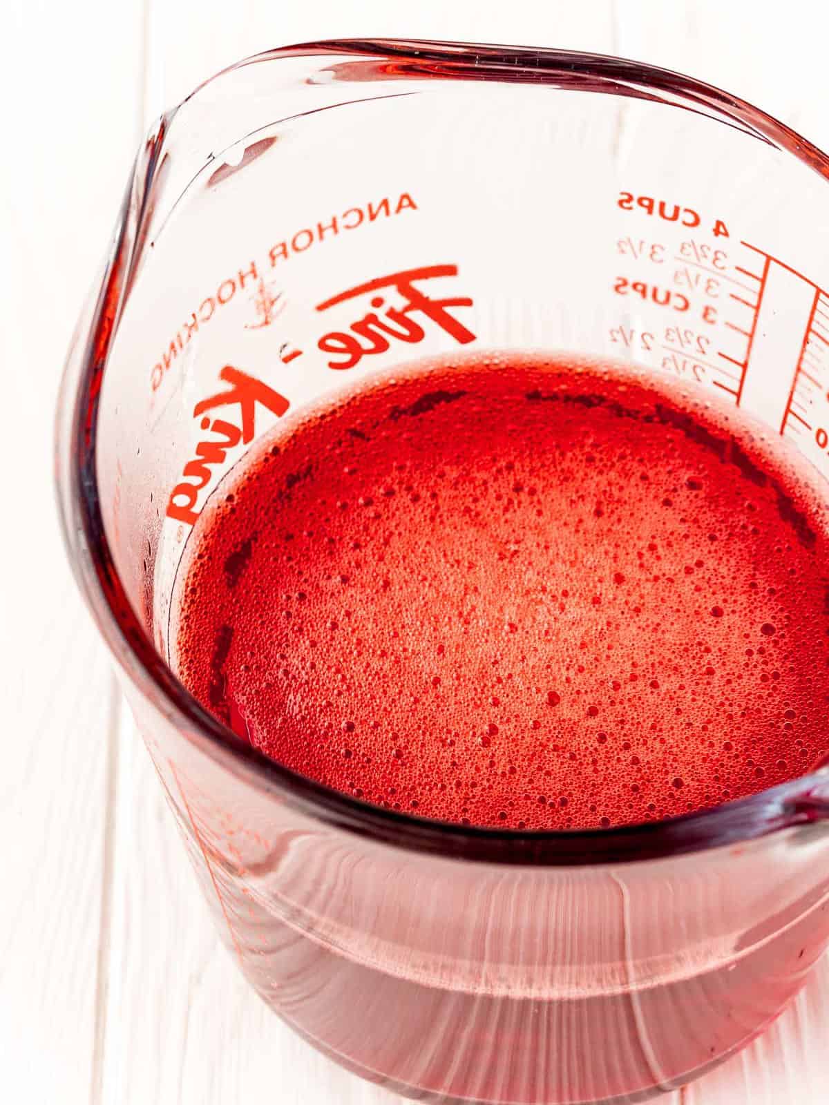 Raspberry Jello dissolved in a measuring cup for Raspberry Poke Cake.