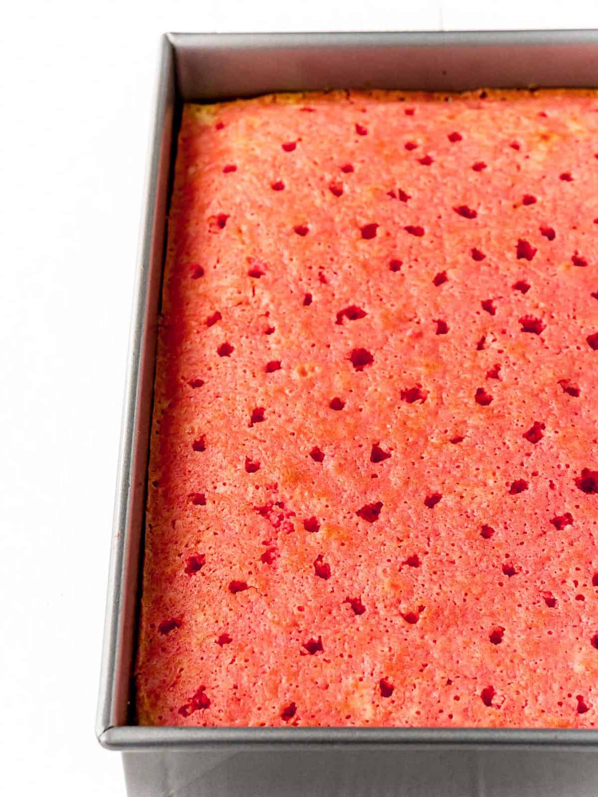Pouring raspberry Jello over the poked cake for Raspberry Poke Cake.
