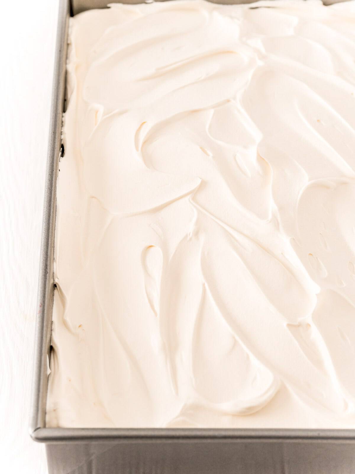 Spreading whipped topping over Raspberry Poke Cake.