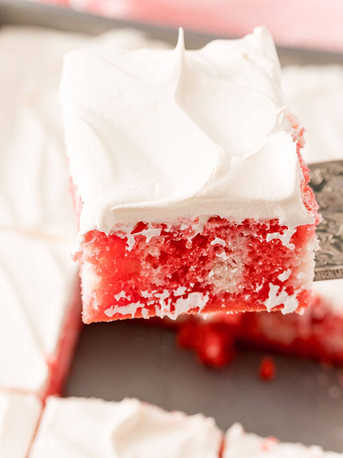 Sliced Raspberry Poke Cake topped with whipped cream and raspberries.