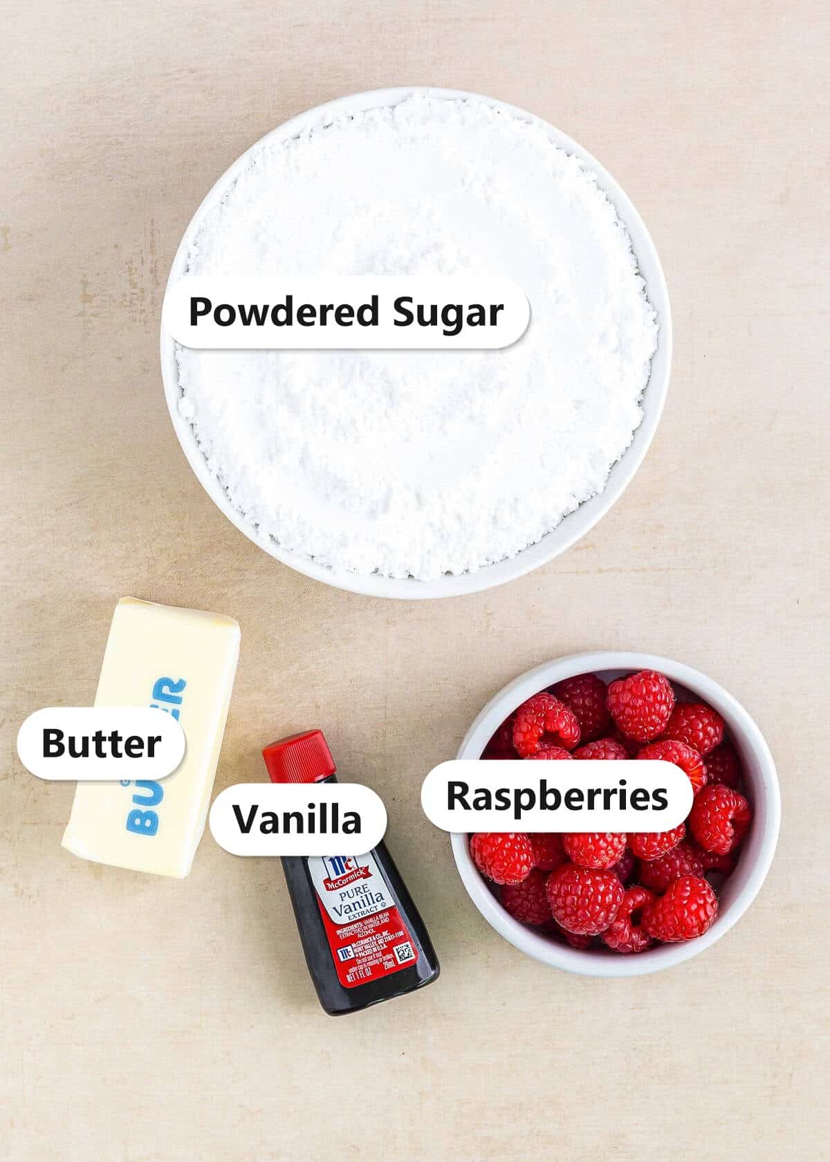 Labeled ingredients to make raspberry frosting including butter, powdered sugar, fresh raspberries, and vanilla.