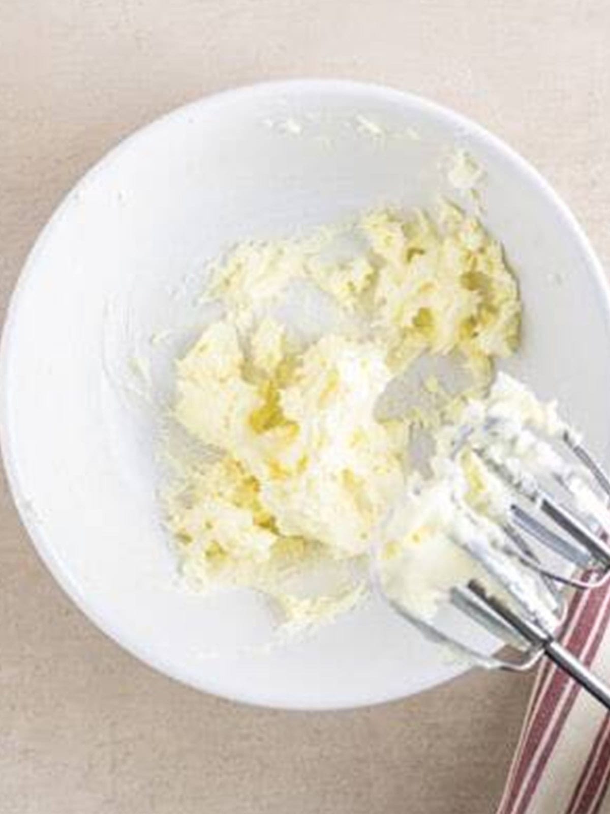 Softened butter whipped smooth in a white bowl with a hand mixer.