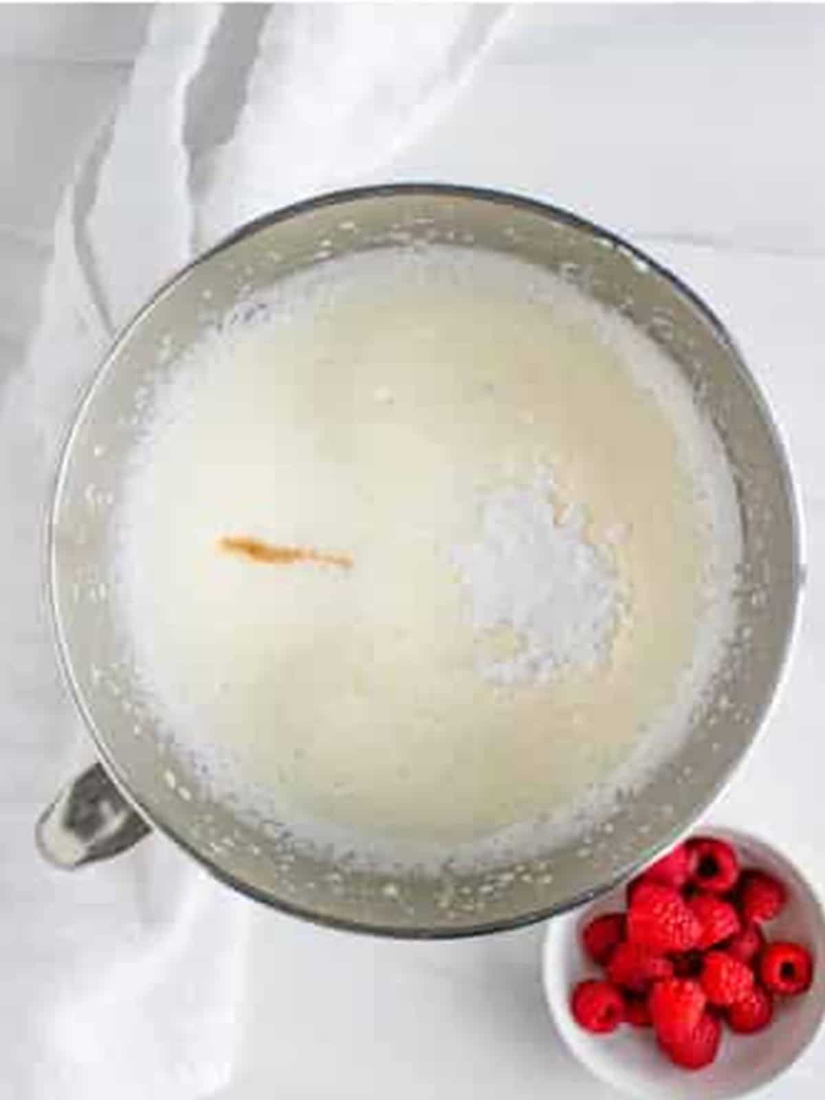 Heavy cream, vanilla, and powdered sugar whipping in a stand mixer bowl for Raspberry Icebox Cake.