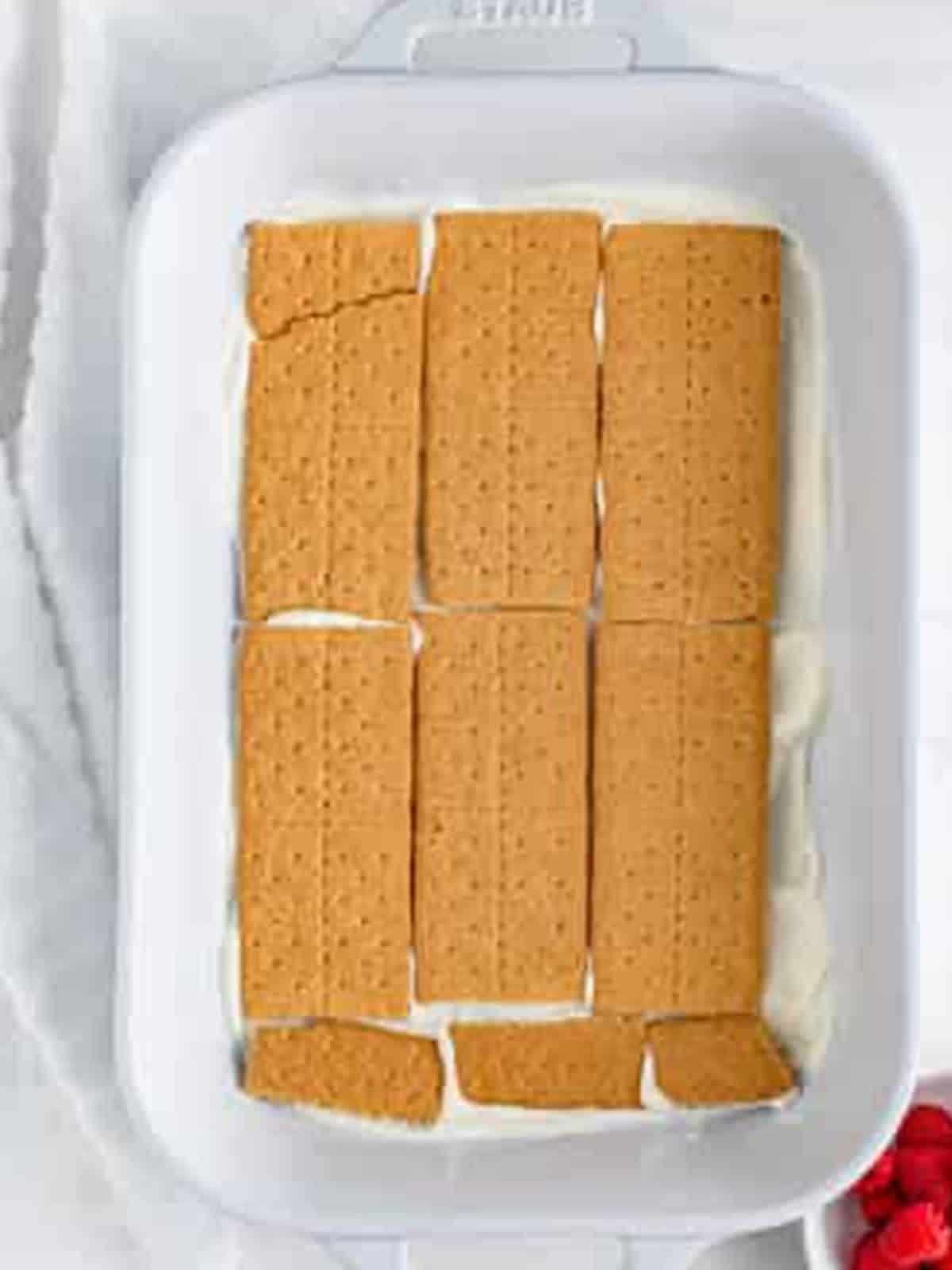 A single layer of graham crackers covering the cream in the dish for Raspberry Icebox Cake.