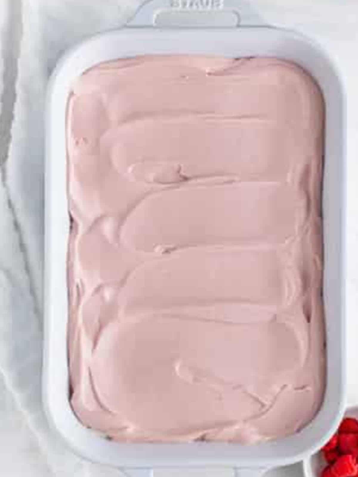 Pink raspberry preserves whipped cream spread over the crackers for Raspberry Icebox Cake.