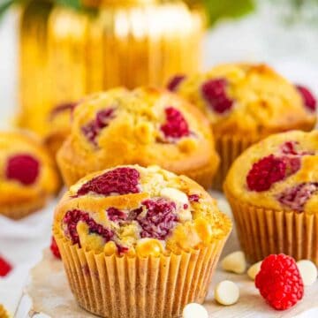 A white chocolate raspberry muffin with a golden top studded with raspberries and white chocolate.