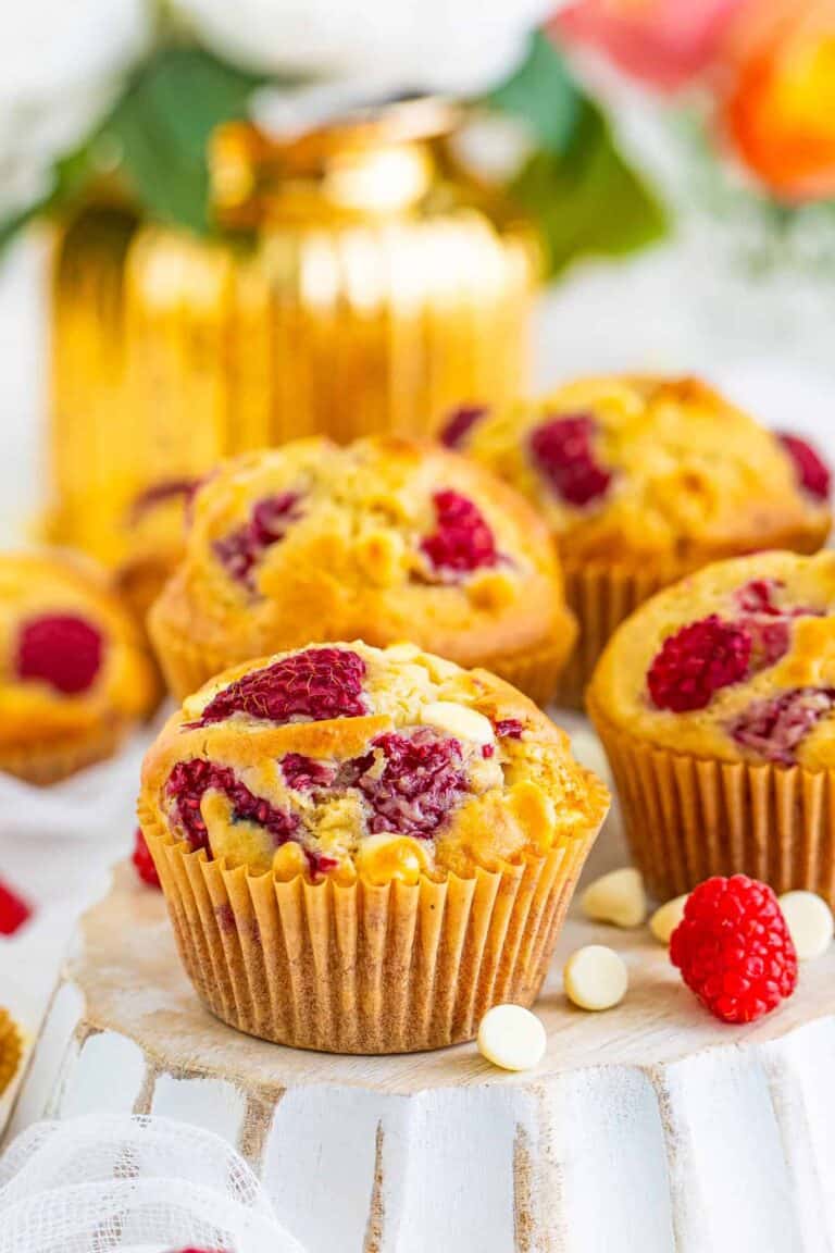 A white chocolate raspberry muffin with a golden top studded with raspberries and white chocolate.