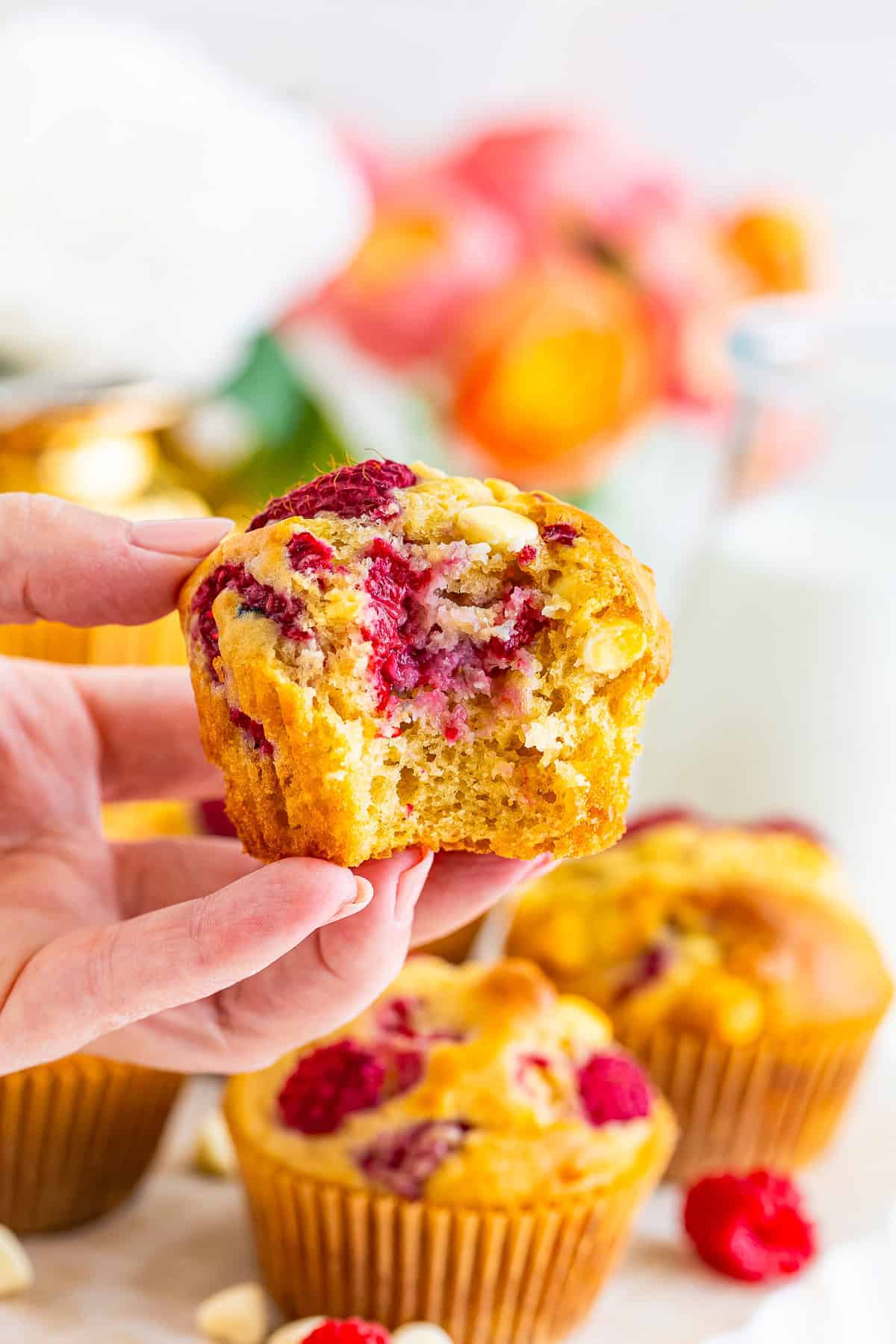 A hand holding a white chocolate raspberry muffin with a bite taken out.