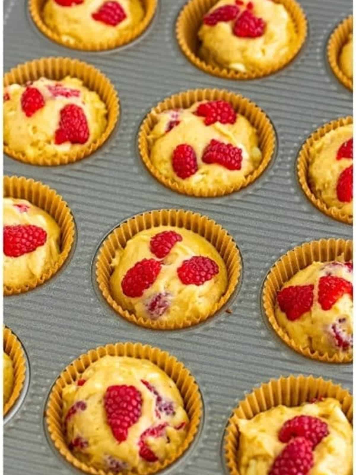 Muffin batter scooped into a lined muffin tin and topped with raspberries.