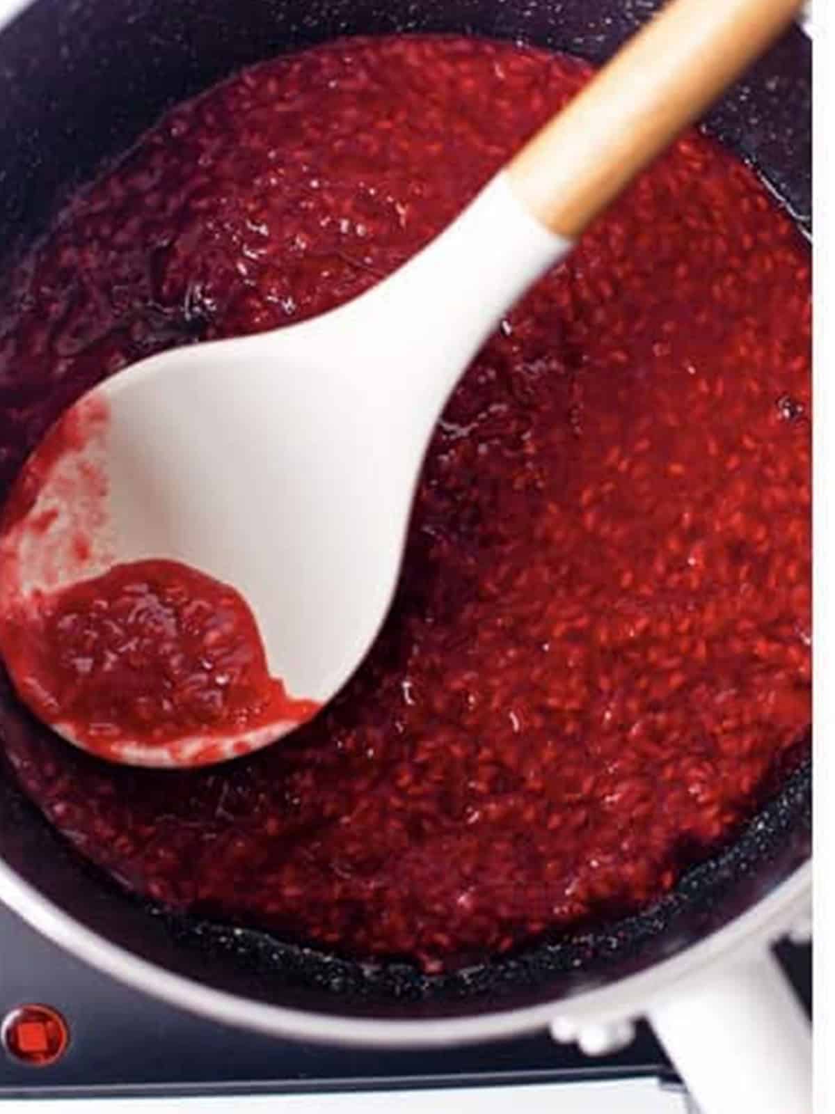 Fresh raspberries cooked down in a saucepan to make raspberry sauce.